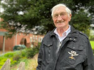 91 year old Jim Wood wearing a black jacket and stood in the gardens of Primrose Hospice