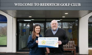 A woman and man stood outside Redditch Golf club with a supporting Primrose Hospice sign.